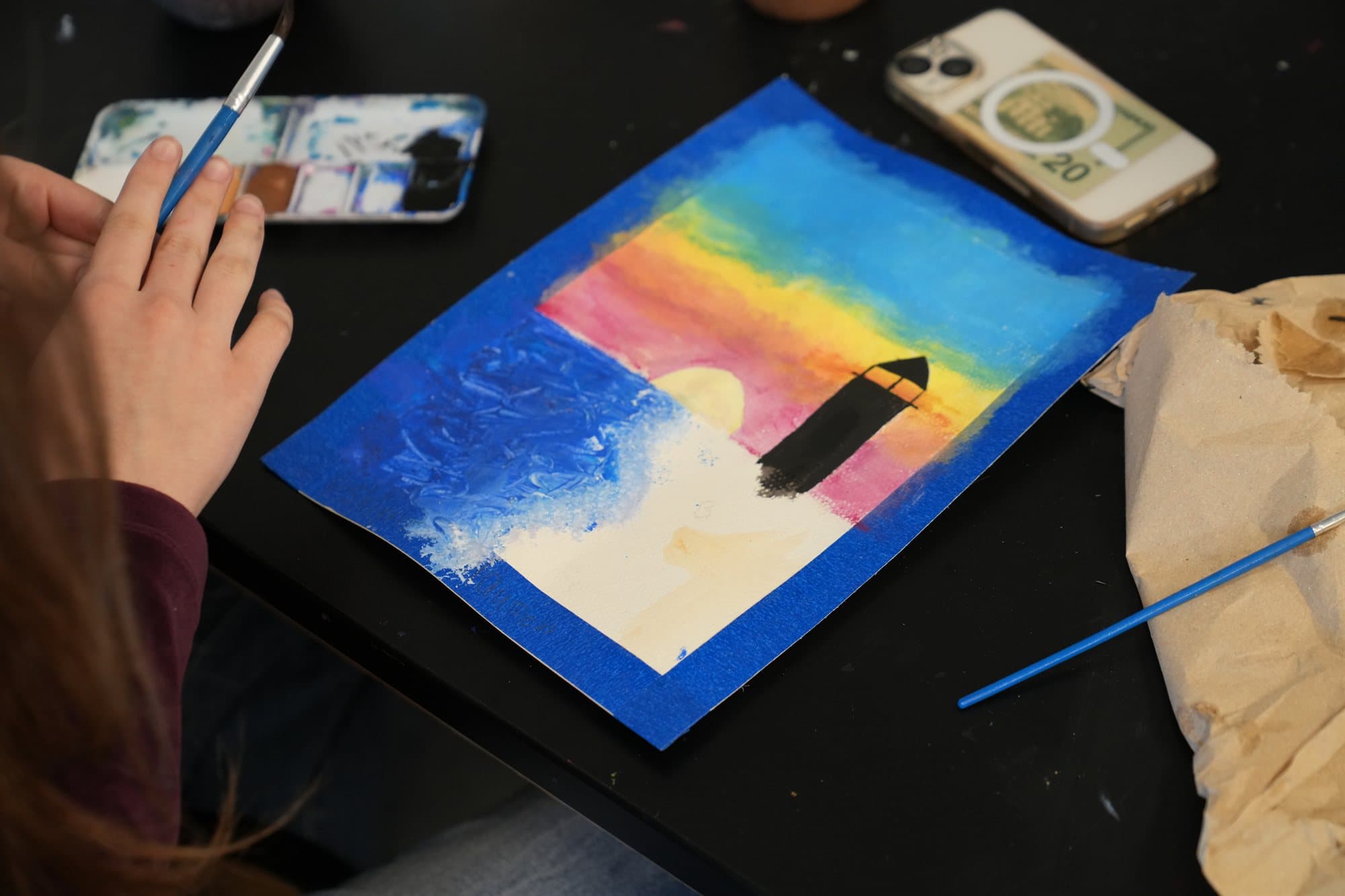 A Highland Prep art student painting a lighthouse at sunset